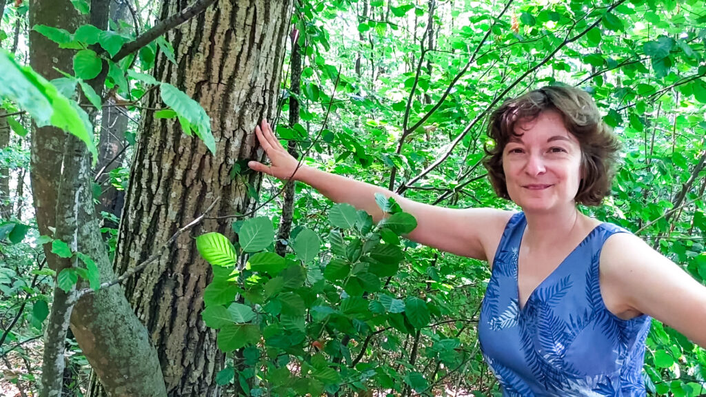 Lesley berührt lächelnd die Rinde eines Baumes im Wald